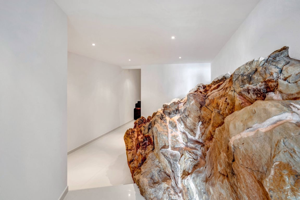 Innenflur mit in die Architektur integrierter natürlicher Felsformation, minimalistischen weißen Wänden und Deckeneinbaustrahlern.