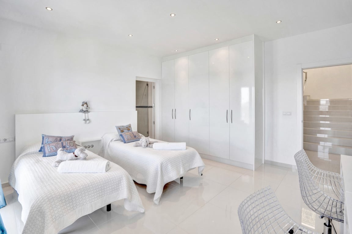 Minimalistisches Doppelzimmer mit hochglänzenden Einbauschränken, polierten weißen Bodenfliesen und direktem Zugang zum En-Suite-Bad.