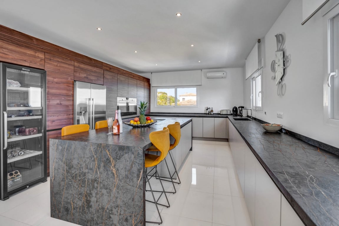 Moderne Küche mit dunkler Steininsel, gelben Barhockern, integrierten Geräten, Weinkühlschrank und hochwertigen Holzfronten.