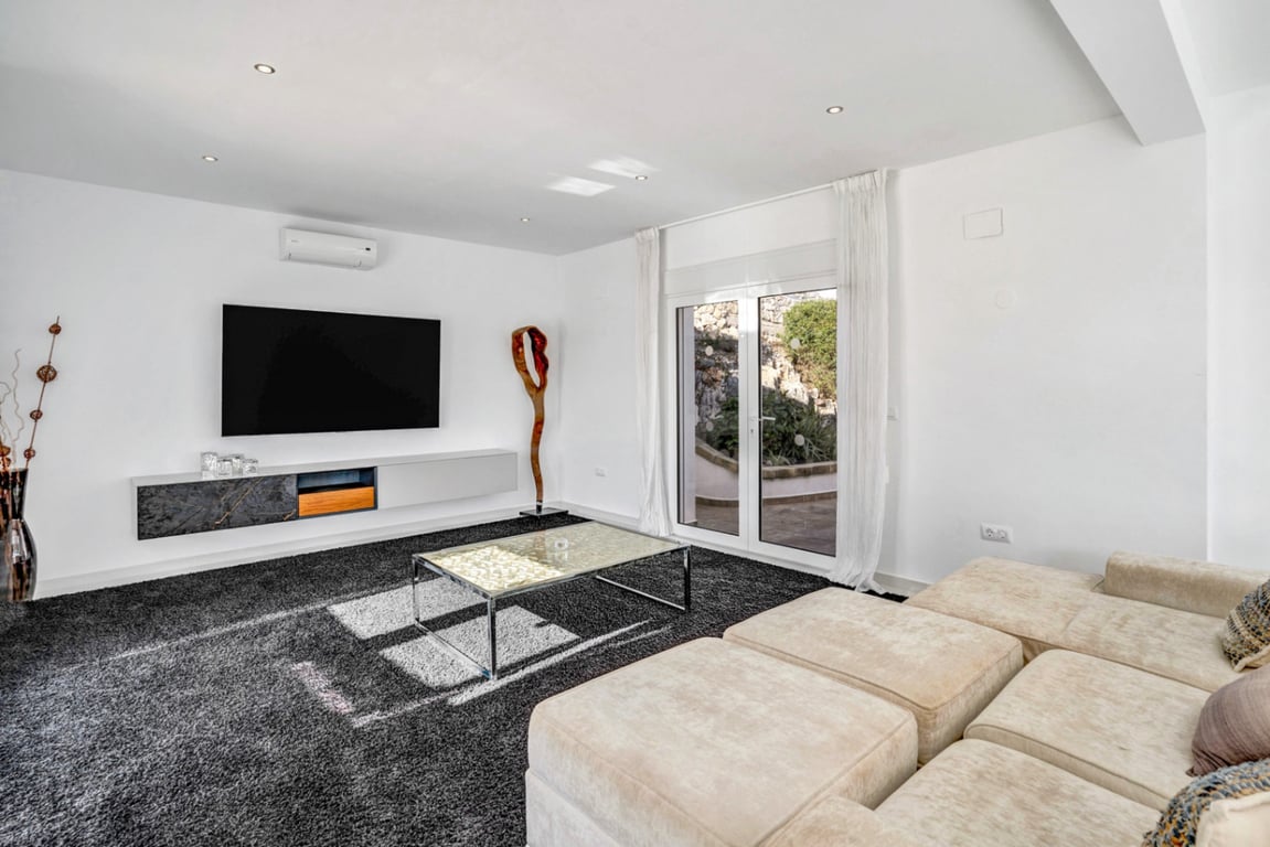 Moderner Medienraum mit modularem Sofa, Hochflor-Teppich und schwebendem Sideboard, inklusive Zugang zur Terrasse und der markanten Felswand.