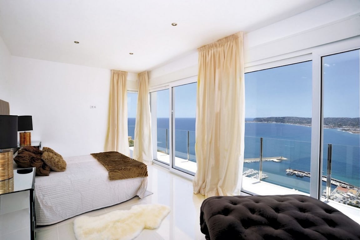 Schlafzimmer-Suite mit bodentiefen Fenstern und Panoramablick auf den Hafen von Jávea. Polierte Böden, Einbaustrahler und direkter Zugang zur Terrasse.