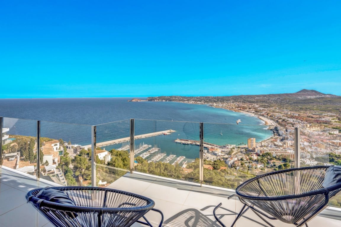 Terrasse mit Glasgeländer und schwarzen Acapulco-Stühlen mit Panoramablick auf den Hafen von Jávea und die Mittelmeerküste.