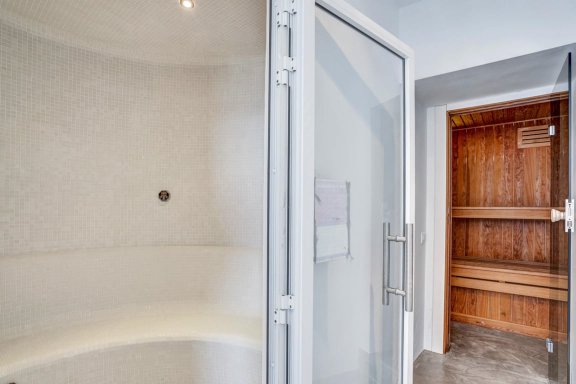 Wellnessbereich mit einem weiß gefliesten Dampfbad und einer angrenzenden finnischen Sauna aus Naturholz für maximale Entspannung.
