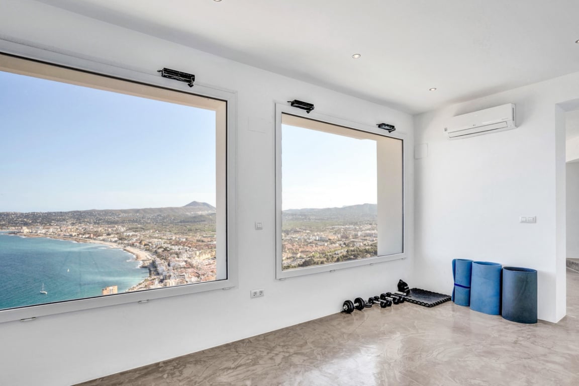 Yoga- und Fitnessbereich mit poliertem Mikrozementboden und großen Panoramafenstern mit weitem Blick über die Bucht von Jávea und das Meer.