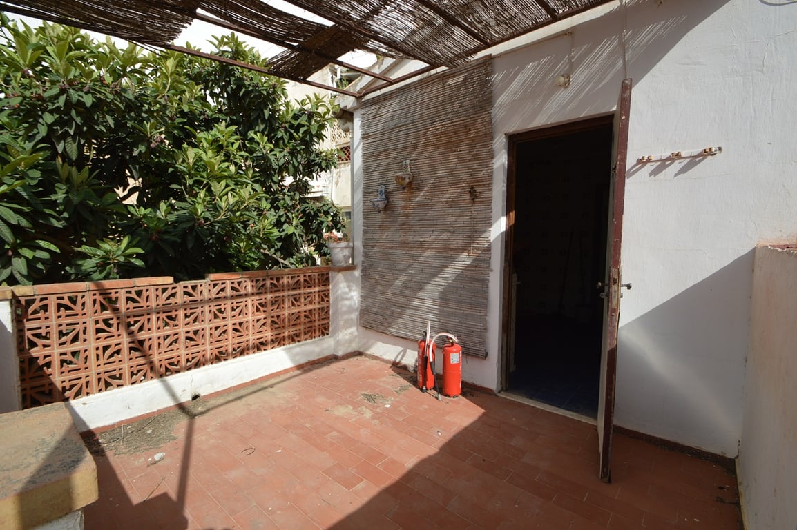 Außen-Terrasse mit Terrakotta-Fliesen, einer Schilfrohr-Pergola und einer dekorativen Gittersteinmauer neben üppiger mediterraner Bepflanzung.