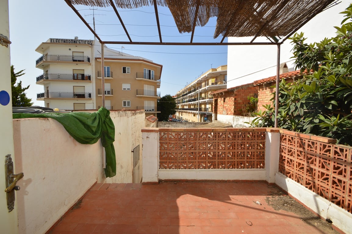 Außenterrasse mit Terrakottaboden und dekorativem Gittermauerwerk unter einer Metallpergola mit Schilfrohrabdeckung und Blick auf die Stadt.