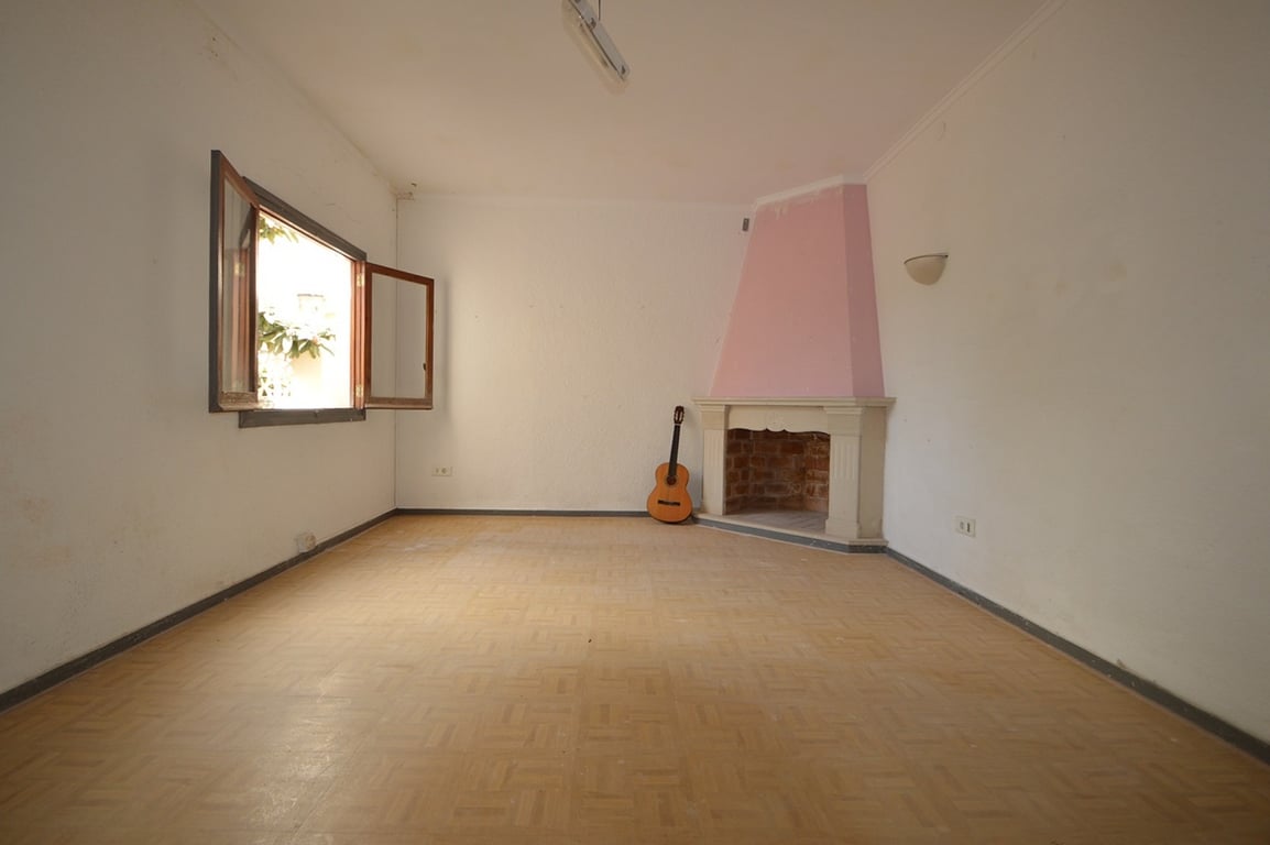 Geräumiges Zimmer mit einem rosa Eckkamin, Parkettboden und einem Holzfenster, das den Blick ins Grüne freigibt.