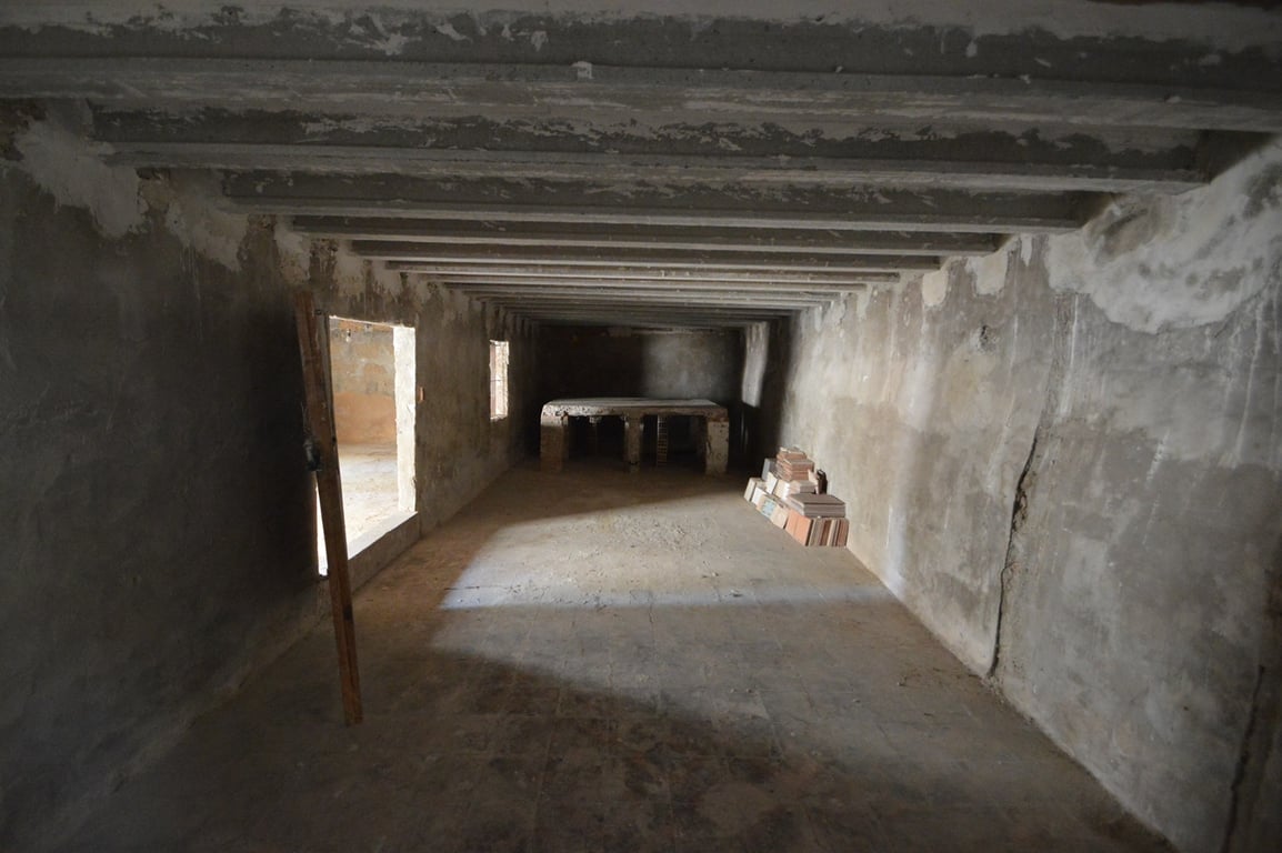 Großer Rohbauraum mit sichtbaren Betonbalken, Steinwänden und einer gemauerten Bank, der sich ideal als Werkstatt oder Lagerraum eignet.