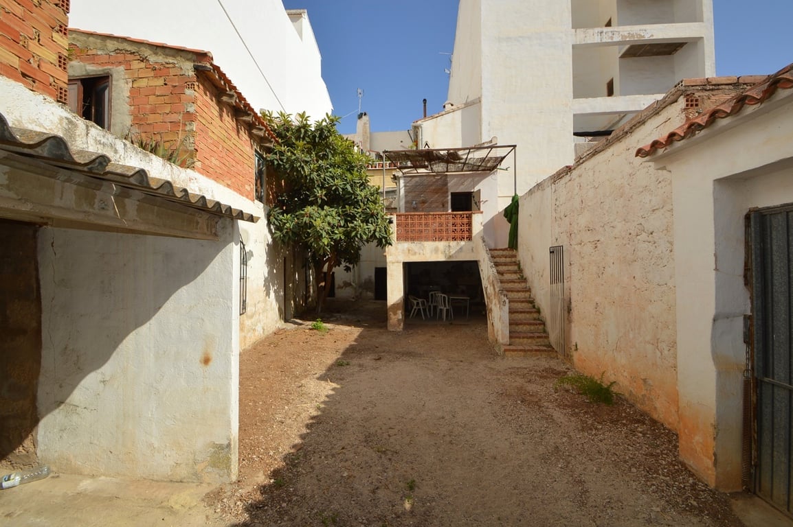 Privater Innenhof mit Erdboden, hohen Mauern und einer Außentreppe, die zu einer erhöhten Terrasse und einem schattigen, überdachten Bereich führt.