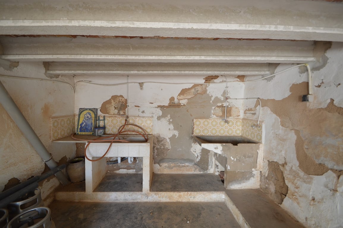 Rustikaler Hauswirtschaftsbereich mit originalen Steinbecken, dekorativen Fliesen und Sichtbalken, ideal für ein umfassendes Renovierungsprojekt.