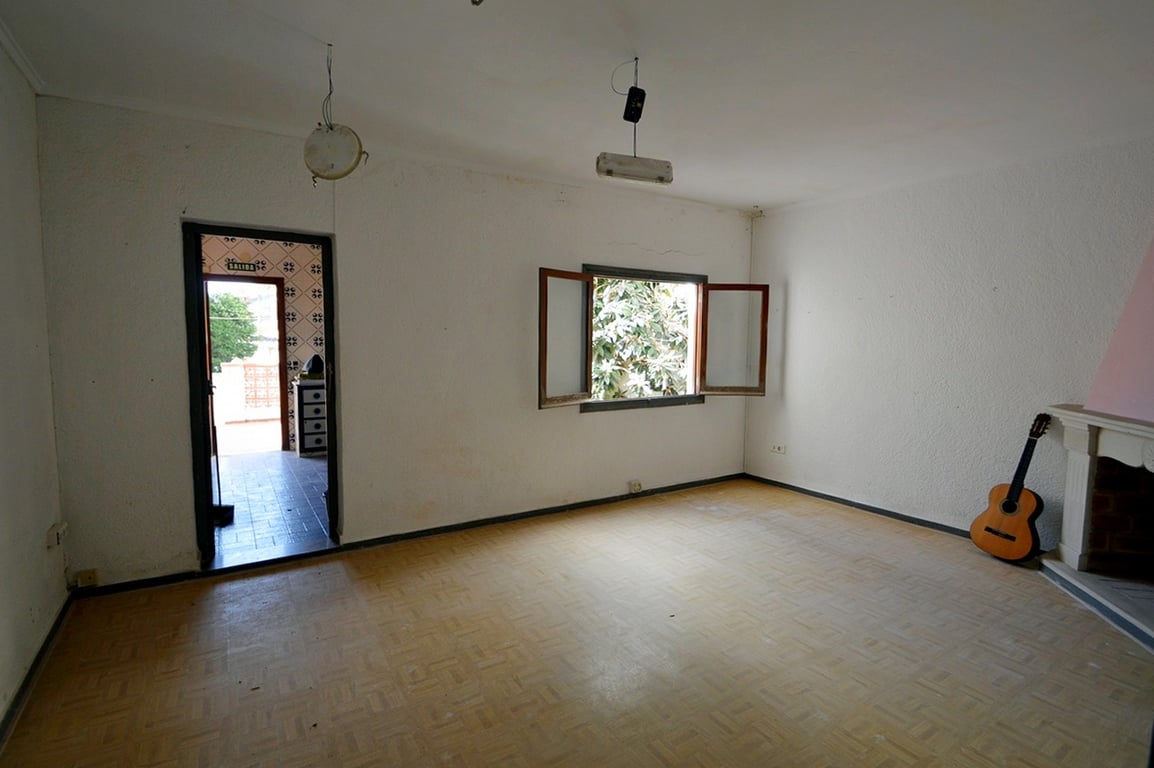 Wohnzimmer mit klassischem Kamin, gemustertem Boden und Fenster zum Garten. Der Raum bietet einen direkten Zugang zum Außenbereich und zur Küche.