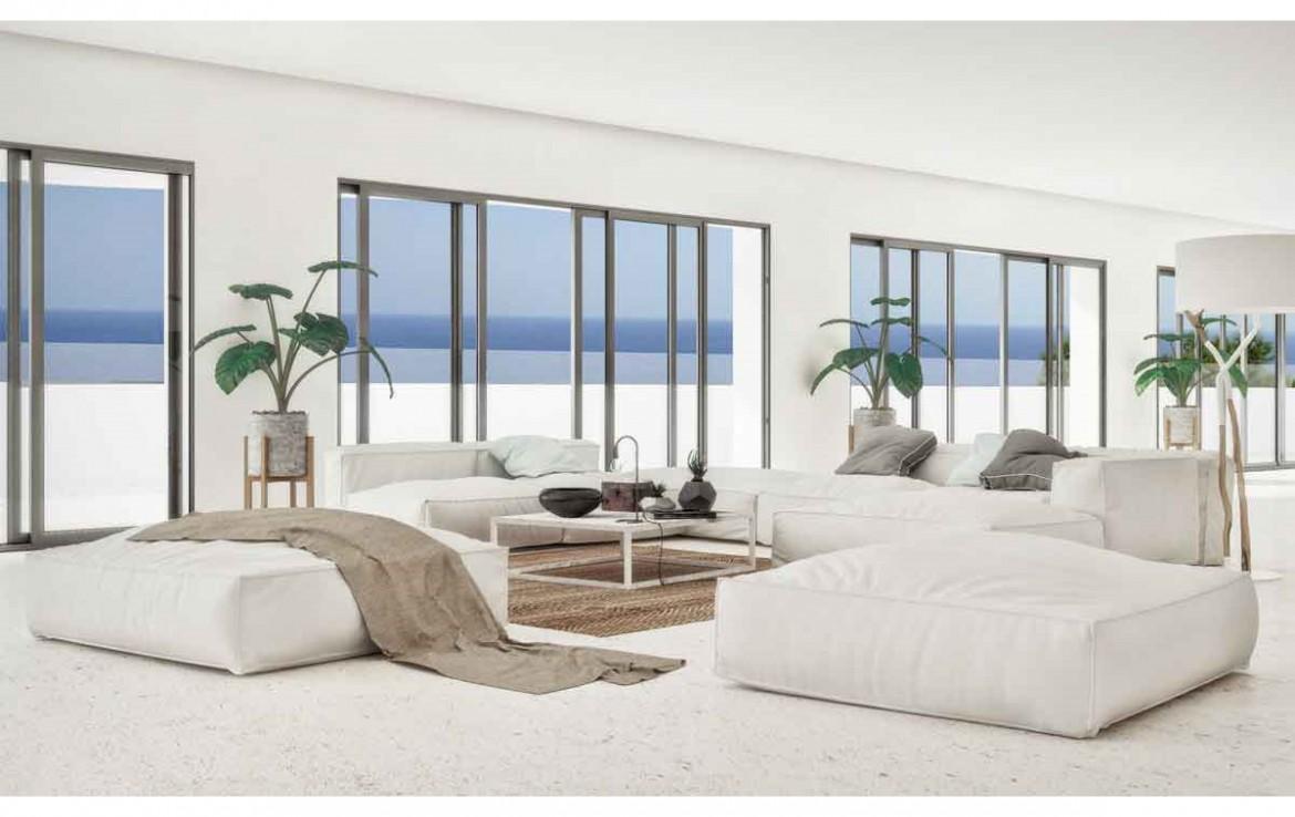 Minimalistischer Wohnbereich mit weißen Modulsofas, hellem Natursteinboden und großen Glasschiebetüren mit direktem Blick auf das Mittelmeer.