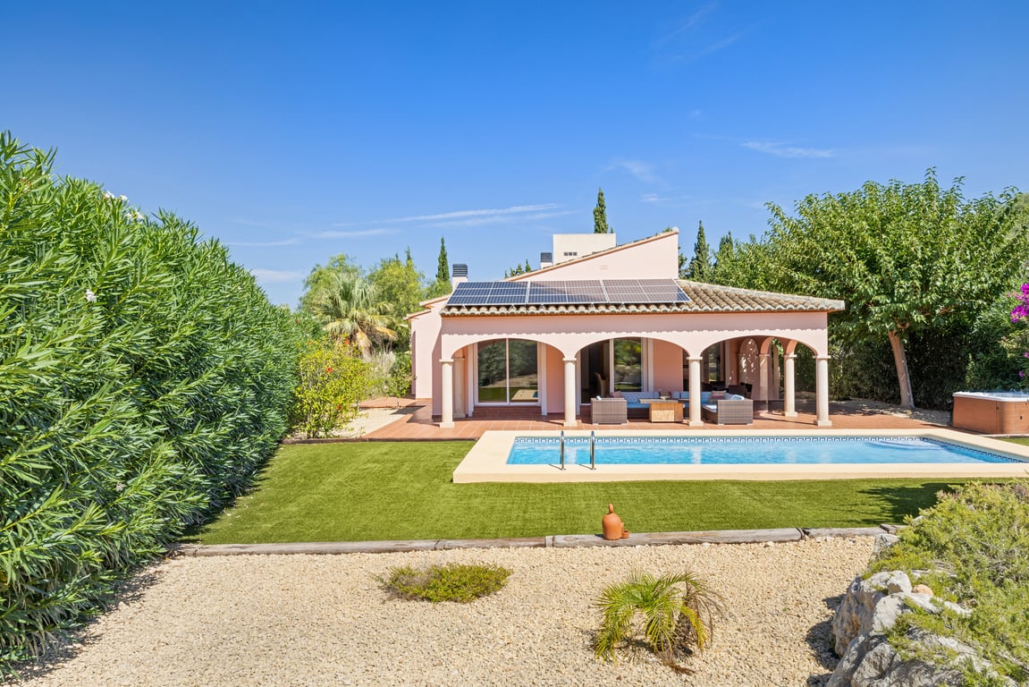Außenansicht der Villa mit privatem Pool, bogenförmiger Naya und Solarmodulen auf dem Dach, eingebettet in einen pflegeleichten Garten mit hohen Hecken.