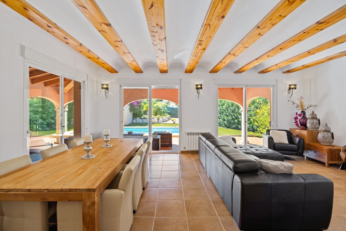 Heller Wohn- und Essbereich mit traditionellen Holzbalkendecken, Terrakottaböden und großen Glasschiebetüren, die direkt zur Naya und zum Pool führen.