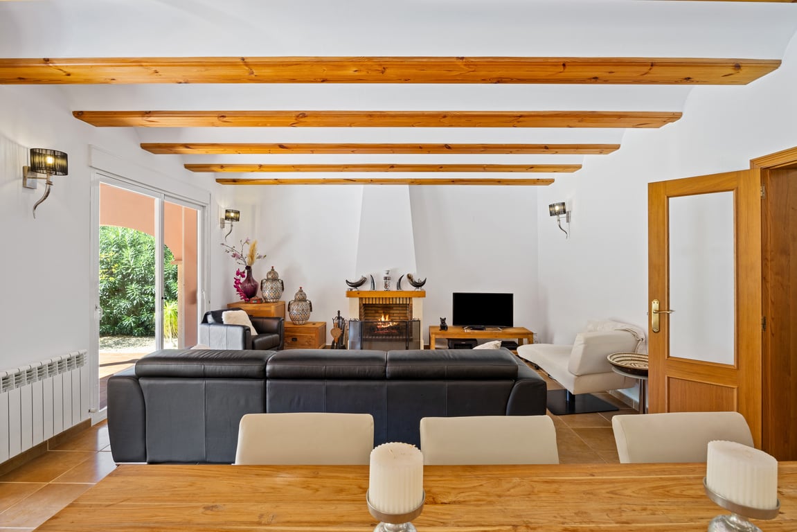 Helles Wohnzimmer mit sichtbaren Holzbalkendecken, zentralem Kamin und Glasschiebetüren zur Naya. Ausgestattet mit Keramikböden und Wandheizkörpern.