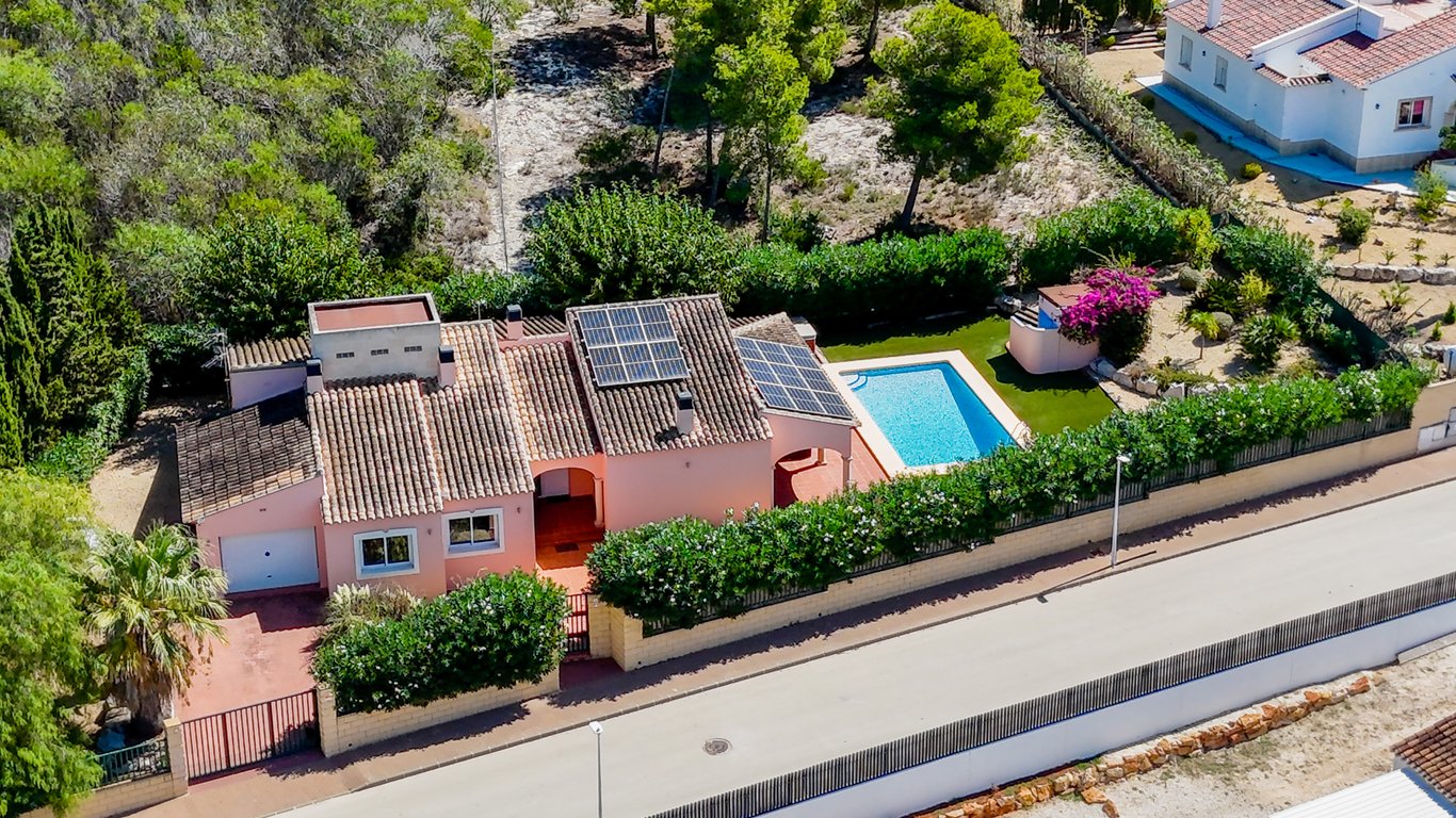 Luftaufnahme der Villa mit Photovoltaikanlage auf dem Ziegeldach, privatem Pool, Kunstrasen und komplett eingefriedetem Grundstück mit Garage und Zufahrt.