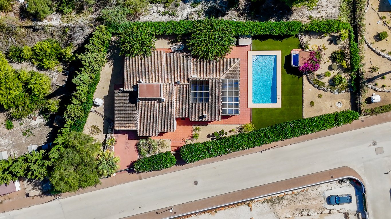 Luftaufnahme der Villa mit Solarmodulen auf dem Ziegeldach, rechteckigem Pool, Kunstrasen und einem privaten Whirlpool-Bereich, umgeben von hohen Hecken.