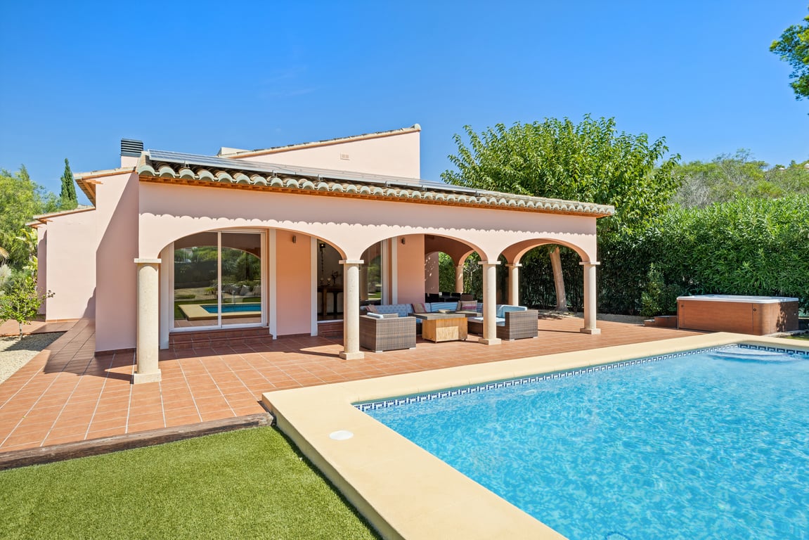 Außenansicht der Villa mit bogenförmiger Naya, Steinsäulen, Terrakotta-Terrasse, Mosaikpool, Solarmodulen auf dem Dach und einem Außen-Whirlpool.
