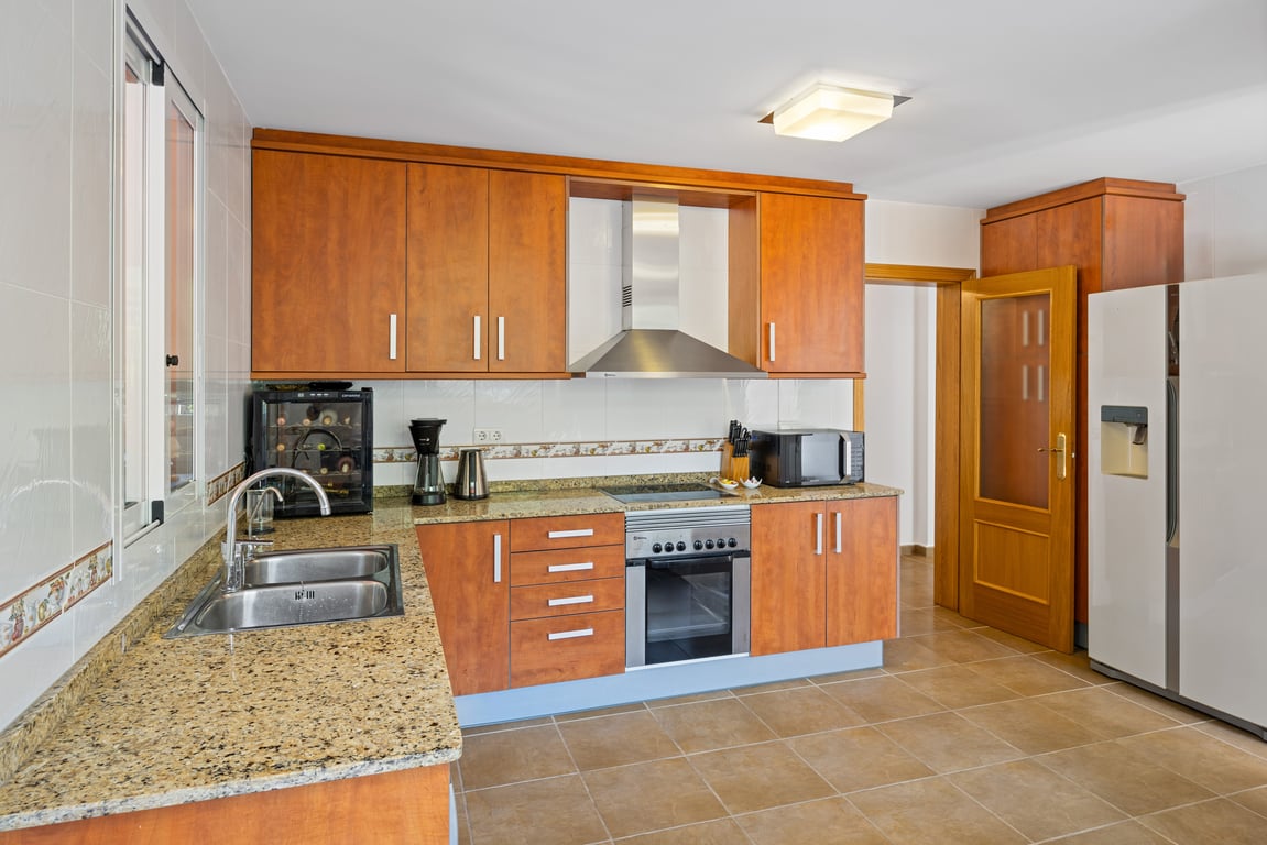 Funktionale Küche mit Holzschränken, gesprenkelten Granitarbeitsplatten, Edelstahlgeräten und einem doppeltürigen amerikanischen Kühlschrank.