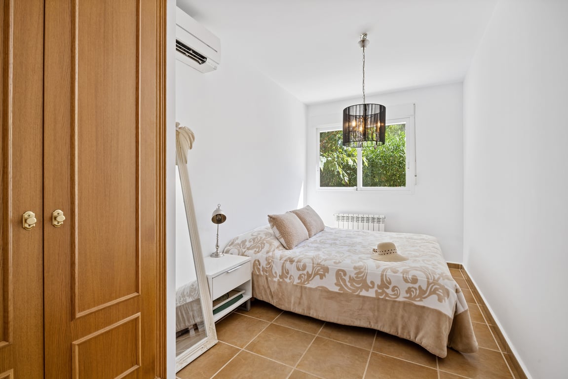 Helles Schlafzimmer mit Terrakotta-Fliesenboden, Split-Klimaanlage, Einbauschrank aus Holz und Fenster mit Blick auf die umliegende Vegetation.