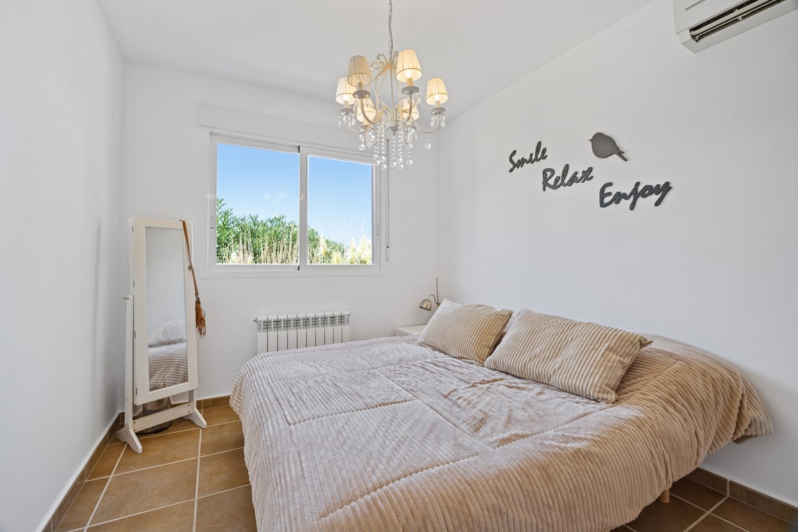 Helles Schlafzimmer mit Terrakotta-Fliesenboden, Split-Klimaanlage und Heizkörper. Es bietet ein doppelt verglastes Fenster mit Blick ins Grüne und einen klassischen Kronleuchter.