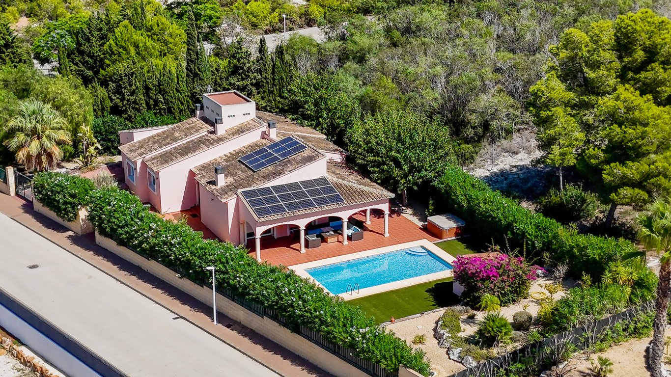 Luftaufnahme der Villa mit Solarmodulen, einer bogenförmigen Naya am Pool und einem gepflegten Garten mit Whirlpool und Kunstrasen.
