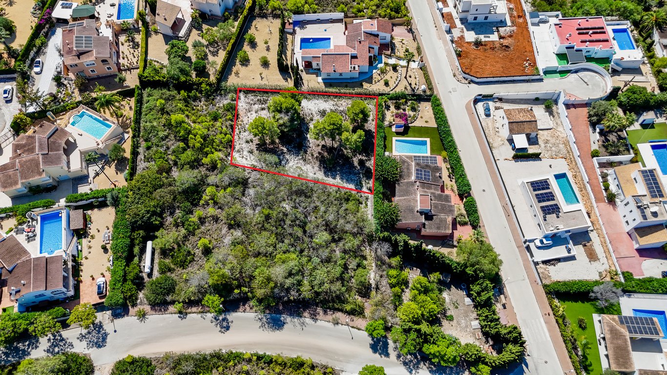 Luftaufnahme des rot markierten Baugrundstücks neben der Villa mit Pool und Solarmodulen, eingebettet in eine ruhige Wohngegend von Jávea.