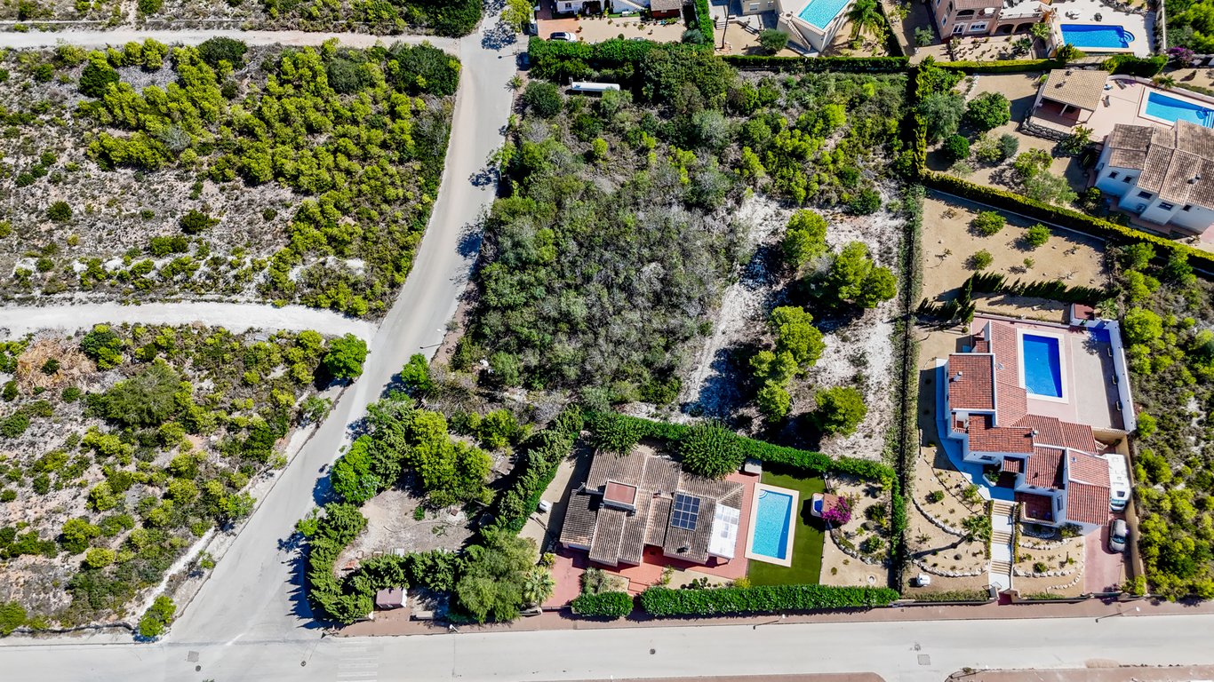 Luftbild der Villa mit Solaranlagen und Pool sowie dem großen, bewaldeten angrenzenden Baugrundstück in einer Wohngegend von Jávea.