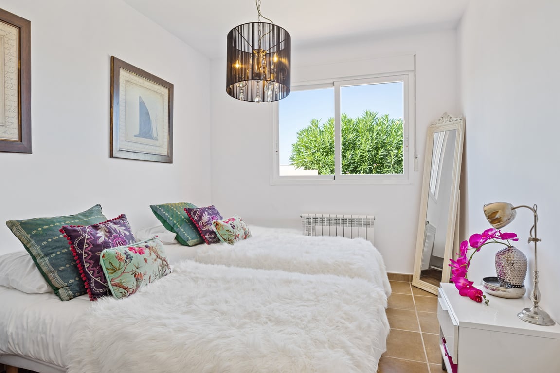 Schlafzimmer mit zwei Einzelbetten, flauschigen weißen Decken, schwarzem Kristallleuchter und Schiebefenster mit Blick ins Grüne.