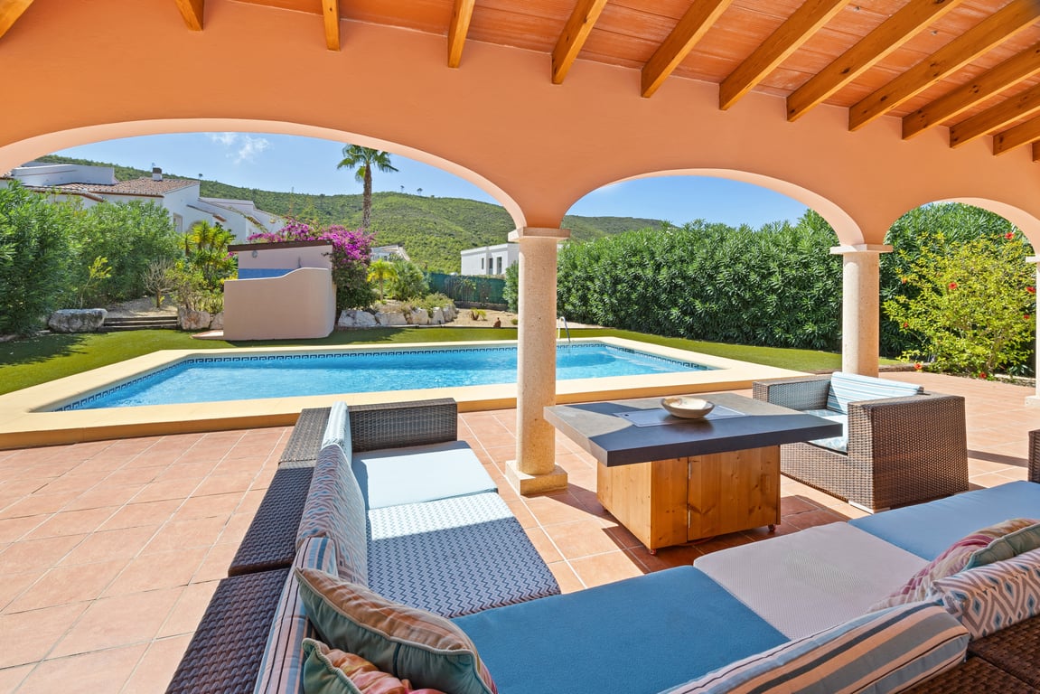 Überdachte Naya mit Holzbalkendecke und Rundbögen, ausgestattet mit Loungemöbeln direkt am Pool mit Blick auf die umliegenden Berge.