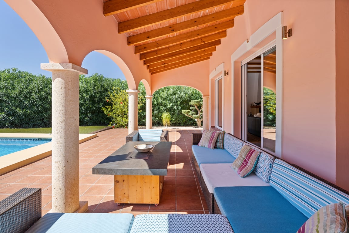 Überdachte Naya mit Sichtbalkendecke, Tosca-Steinsäulen und gemütlichem Loungebereich direkt am Pool und dem mediterranen Garten.