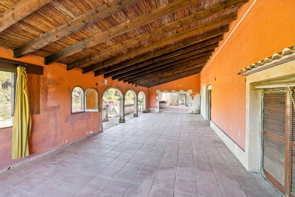 Große überdachte Terrasse mit traditionellen Holzbalken, Schilfrohrdecke, terracottafarbenen Wänden und klassischen Steinbögen zum Außenbereich.