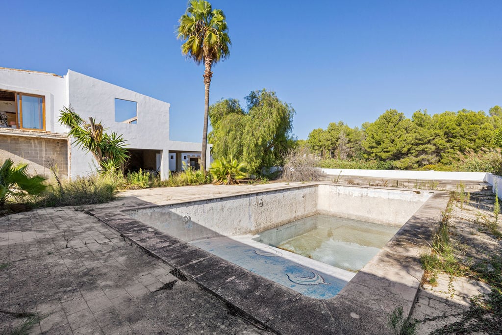 Großer Außenpool mit Mosaikverzierungen und weitläufiger Terrasse, eingebettet in mediterrane Vegetation vor einem weißen, modernen Gebäude.