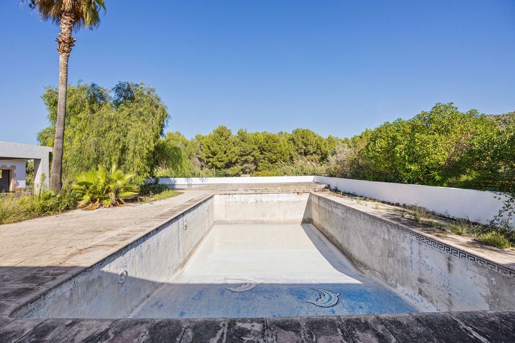 Großes, rechteckiges Schwimmbecken mit Mosaikdetails und weitläufiger Steinterrasse, eingebettet in eine mediterrane Gartenlandschaft mit Pinien und Palmen.