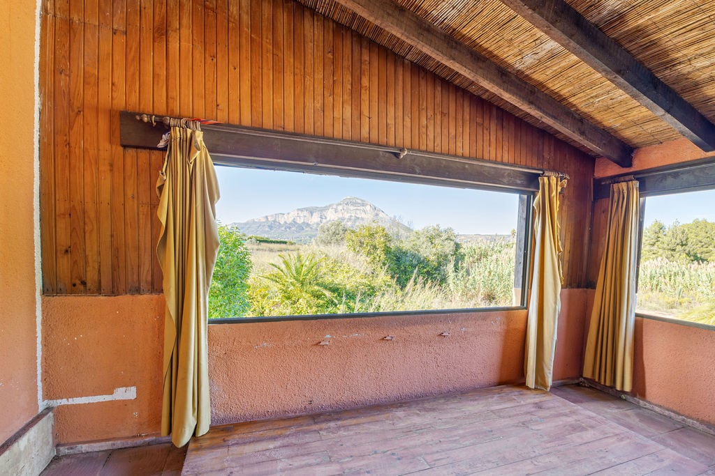 Innenraum mit Holzverkleidung und Schilfrohrdecke, der durch ein breites Panoramafenster einen direkten Blick auf das Montgó-Massiv bietet.