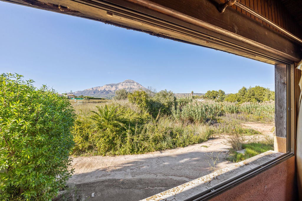 Panoramablick auf den Berg Montgó durch ein Fenster mit Holzrahmen. Die Umgebung besticht durch mediterrane Vegetation und einen weiten, klaren Himmel.