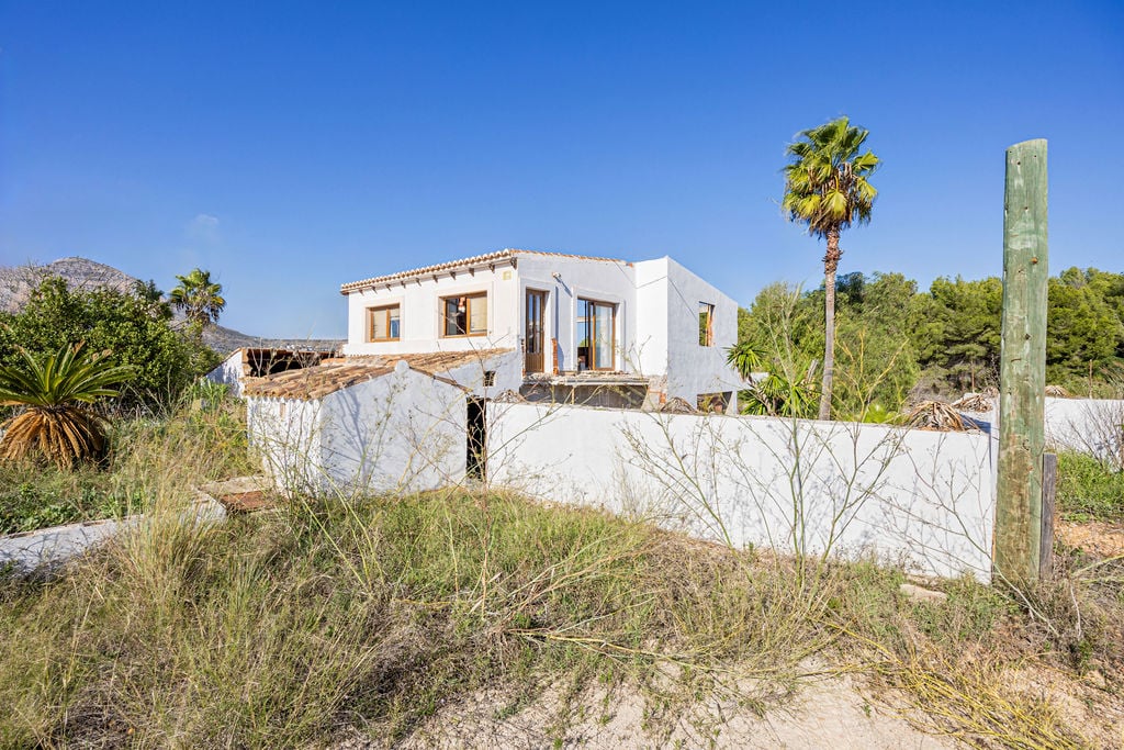 Traditionelle mediterrane Fassade mit weiß getünchten Wänden, Terrakotta-Ziegeldächern und natürlicher Vegetation vor klarem blauem Himmel.
