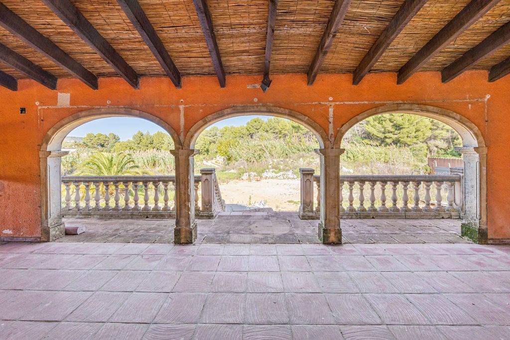 Überdachte Terrasse mit Rundbögen aus Naturstein, Holzbalkendecke mit Schilfrohr-Verkleidung und Blick auf die umliegende mediterrane Landschaft.