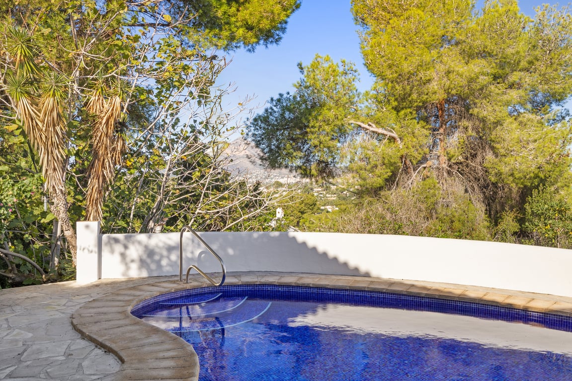 Blau gefliester Pool mit Metalleinstieg, umgeben von einer Natursteinterrasse und mediterraner Bepflanzung mit Blick auf das Montgó-Massiv.