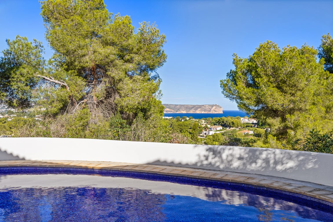 Blick vom privaten Pool auf das Mittelmeer und die Küstenfelsen, eingerahmt von Pinien und einer geschwungenen weißen Mauer.
