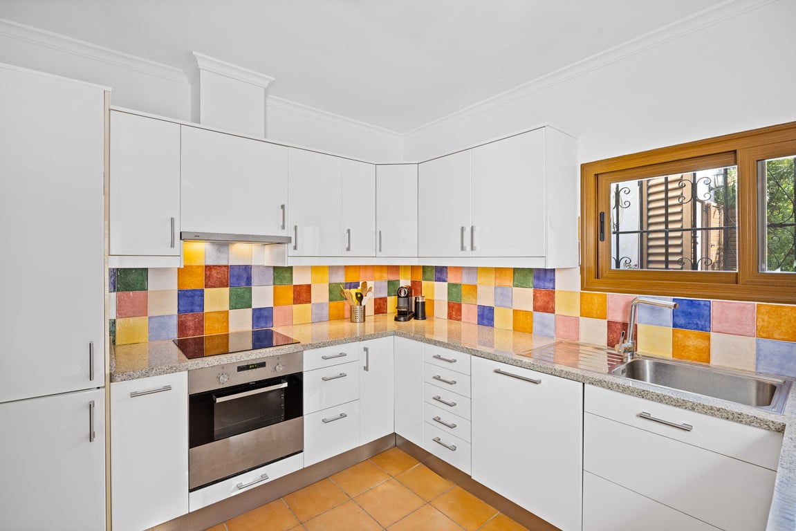 Einbauküche mit weißen Schränken, Granitarbeitsplatte und einem farbenfrohen Fliesenspiegel aus handgefertigter Keramik. Mit integriertem Backofen und Holzfenster.