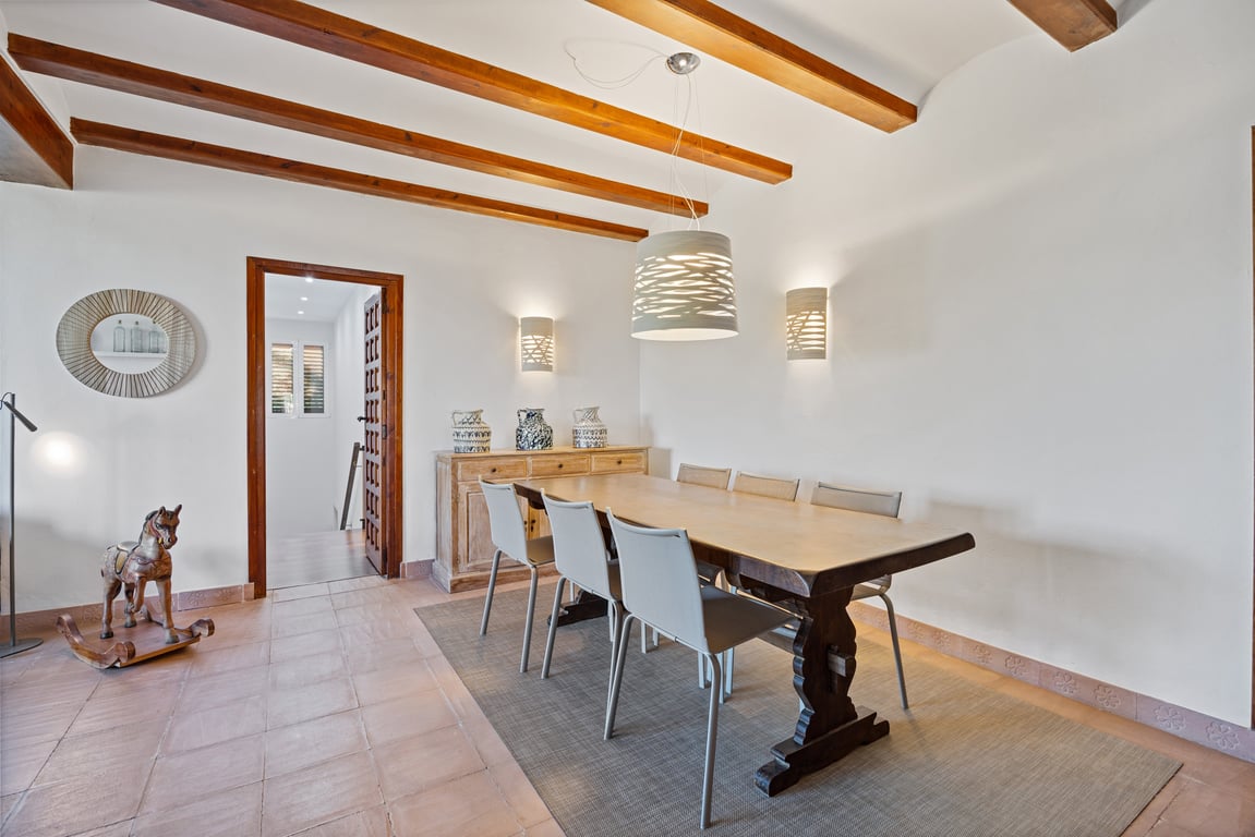 Essbereich mit sichtbaren Holzbalkendecken, traditionellen Keramikfliesen und einem Massivholztisch, akzentuiert durch moderne Designerleuchten.