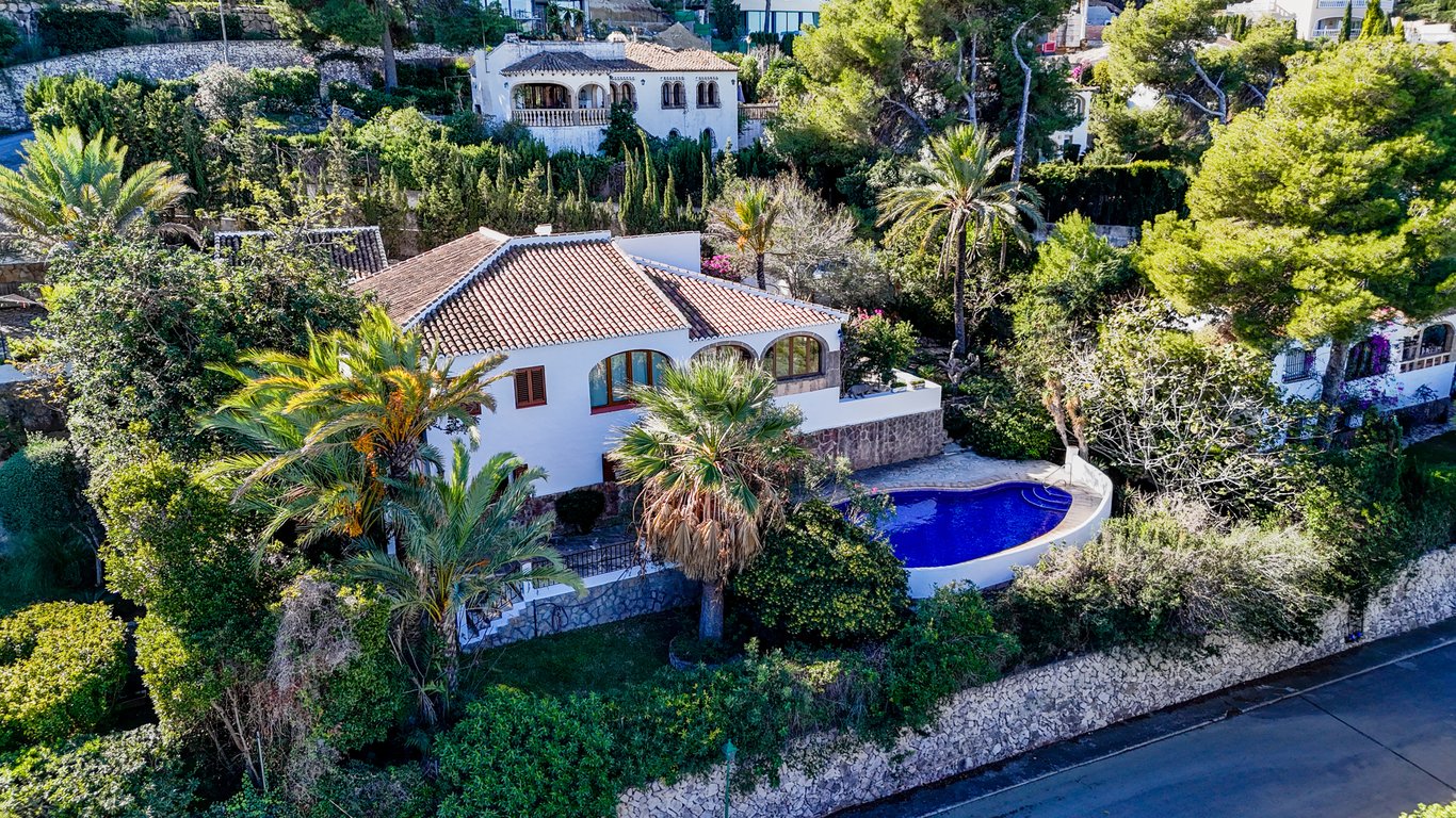 Luftaufnahme der traditionellen Villa mit nierenförmigem Pool, bogenförmiger Naya und üppigem mediterranem Garten, umgeben von Natursteinmauern.