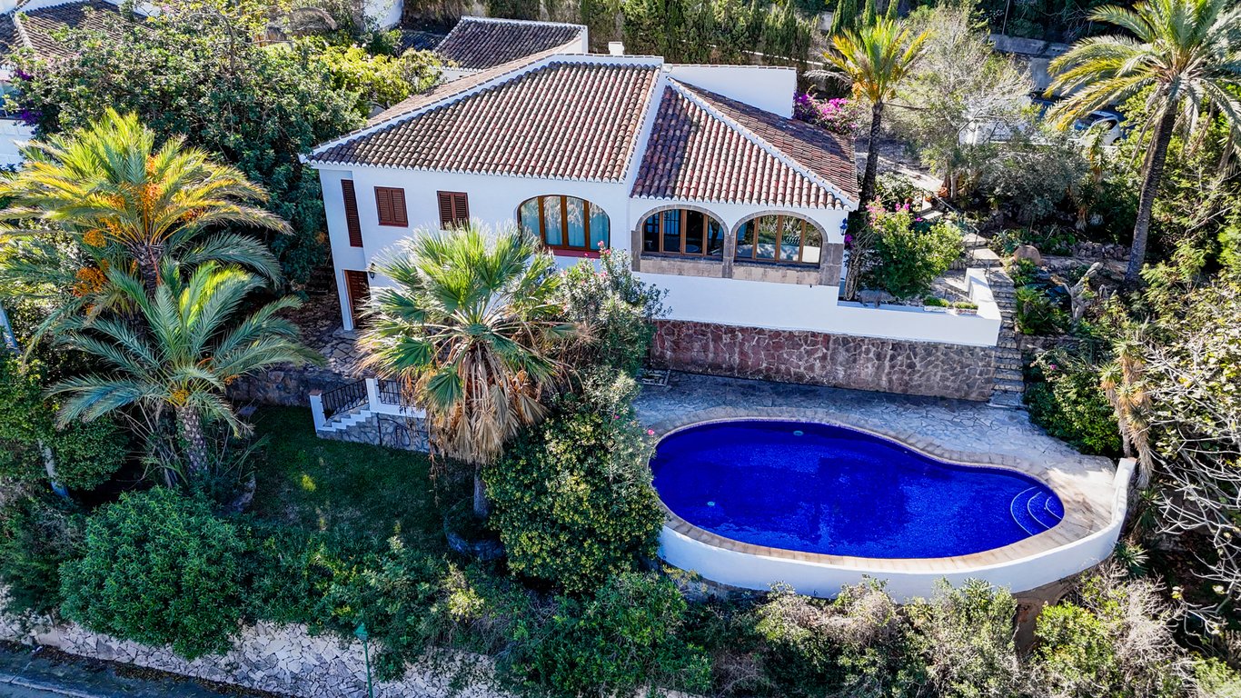 Luftaufnahme der Villa mit nierenförmigem Pool, umgeben von mediterraner Bepflanzung, Palmen und einer traditionellen Naya mit Bögen aus Tosca-Naturstein.