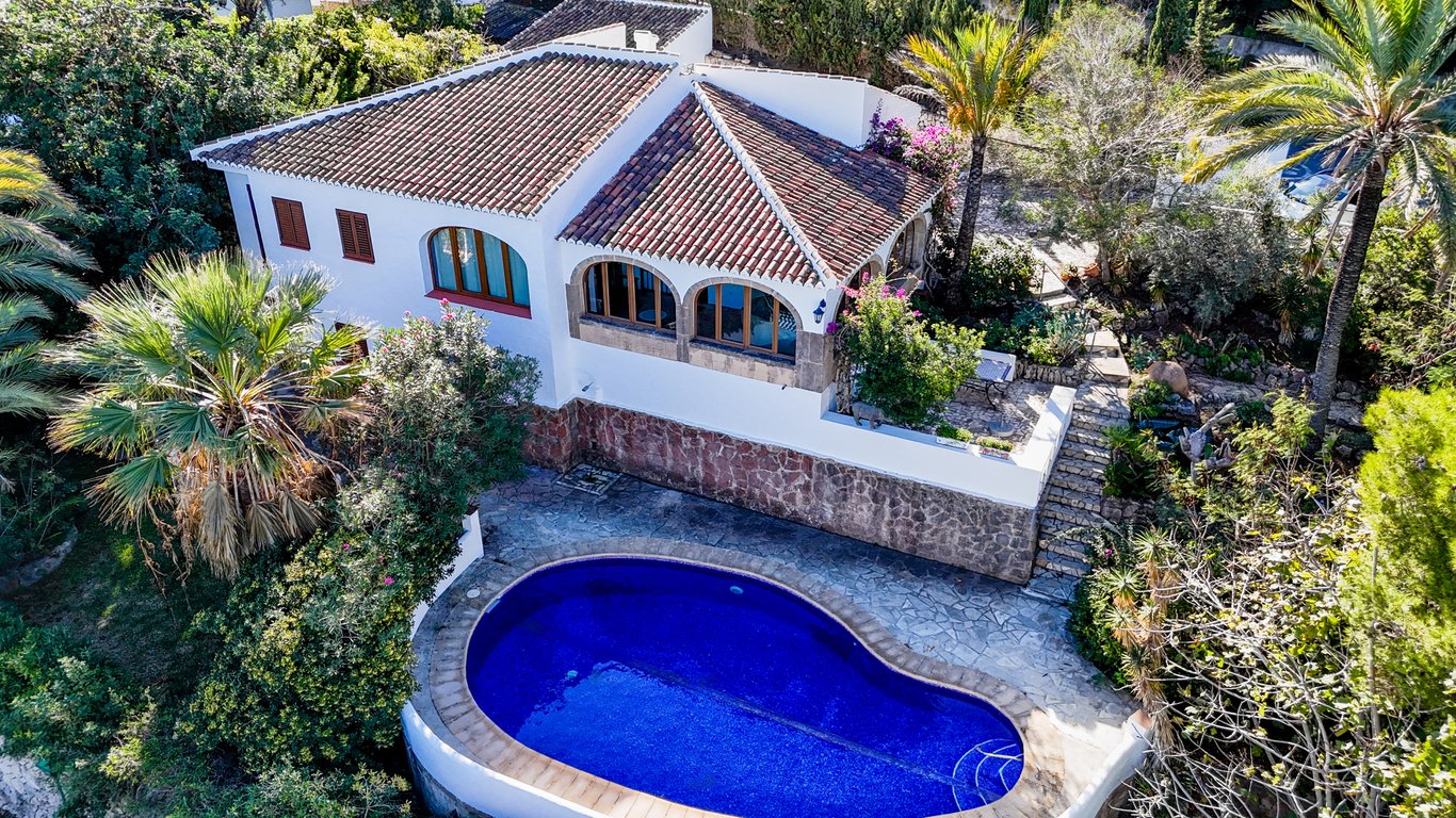 Luftaufnahme der Villa mit nierenförmigem Pool, weißer Fassade mit Natursteinsockel und verglaster Naya mit traditionellen Tosca-Steinbögen.