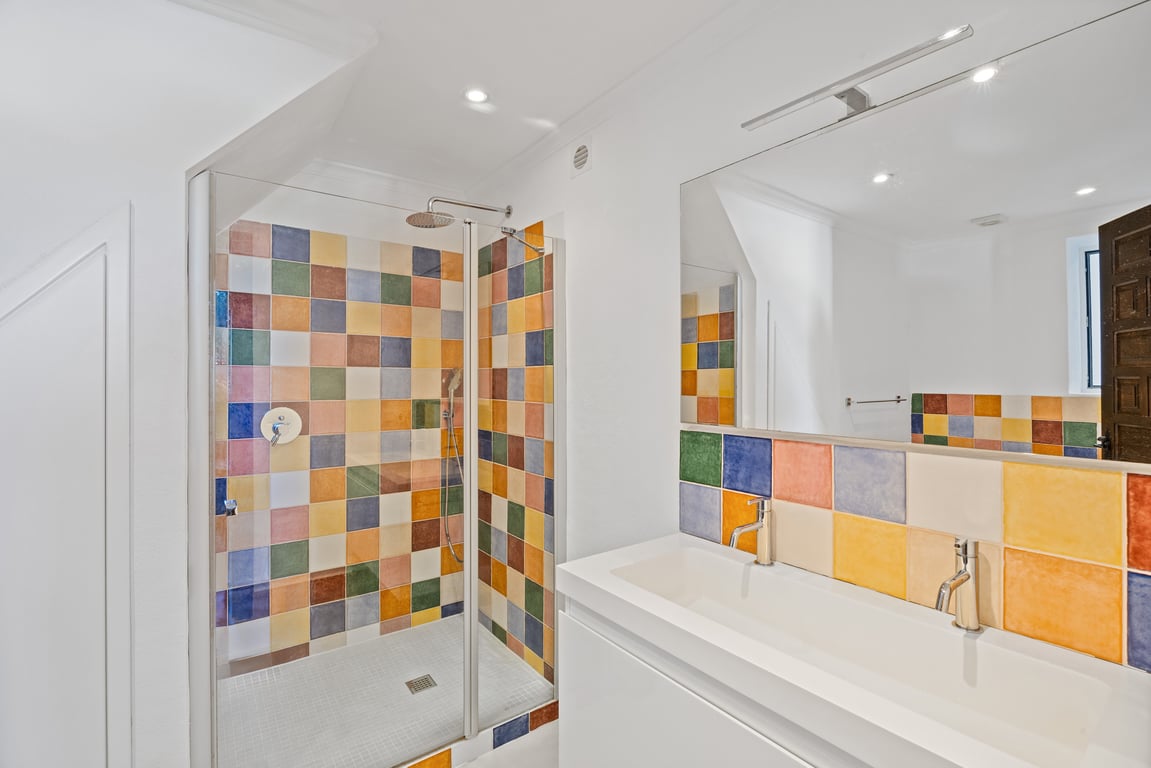 Modernes Badezimmer mit Doppelwaschbecken und Glasduschkabine, akzentuiert durch farbenfrohe Keramikfliesen und integrierte Deckenstrahler.