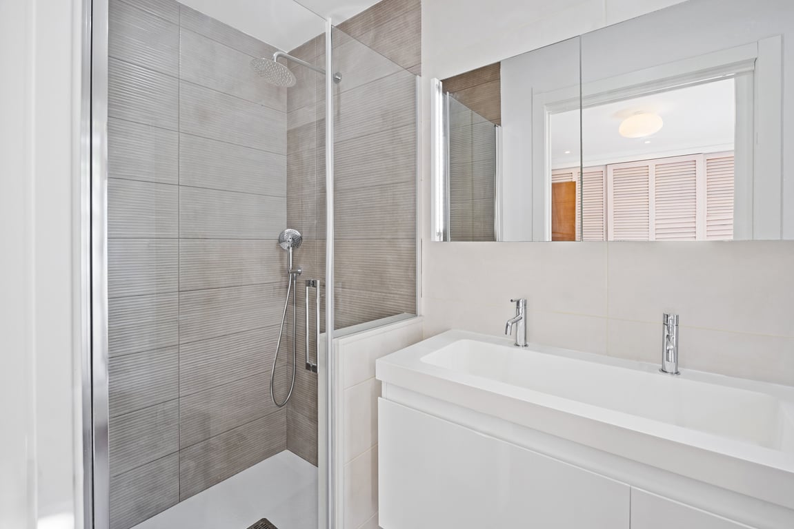 Modernes Badezimmer mit ebenerdiger Dusche, strukturierten grauen Wandfliesen, Glastrennwand und weißem Waschtisch mit zeitgenössischen Chromarmaturen.