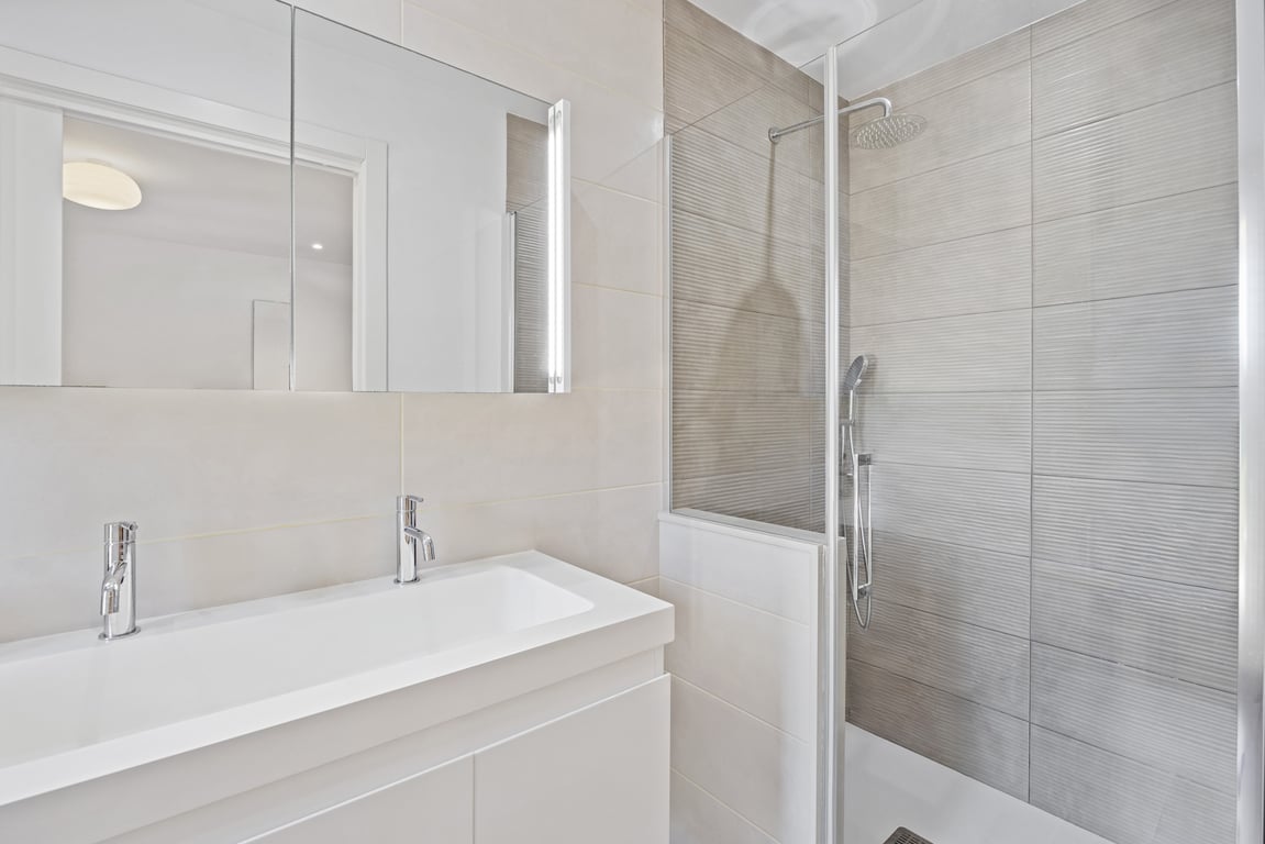 Modernes renoviertes Badezimmer mit Doppelwaschbecken, Spiegelschrank und begehbarer Dusche mit strukturierten grauen Fliesen und Glastrennwand.