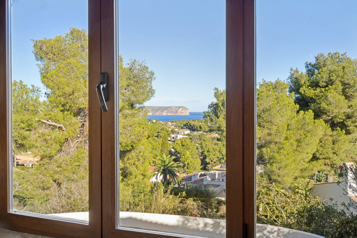 Panoramablick auf das Meer und die Landzunge durch ein Holzoptik-Fenster mit Doppelverglasung, umgeben von mediterranen Pinien.