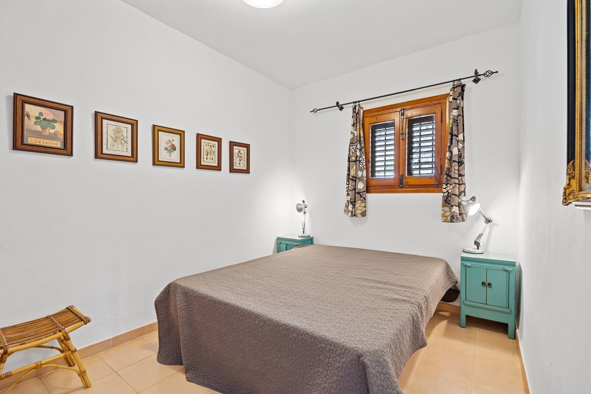 Schlafzimmer mit Doppelbett, türkisfarbenen Nachttischen und Holzfenster mit traditionellen Fensterläden. Weiße Wände mit einer Reihe botanischer Kunstdrucke.